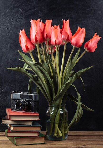 Strauß roter Tulpen und Stapel Bücher mit Filmkamera auf Kreidetafelhintergrund. Schulstillleben