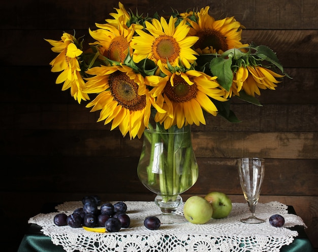 Strauß Sonnenblumen, Pflaumen und Äpfel auf dunklem Hintergrund