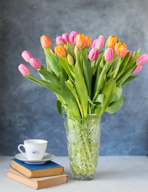 Strauß Tulpen in Vase und Bücher auf dem Tisch. Frühlingsblumen . Blumenstrauß in Vase. Rosa und orange blühende Flora. Gemütliches Stillleben. Speicherplatz kopieren. Urlaubsgruß.