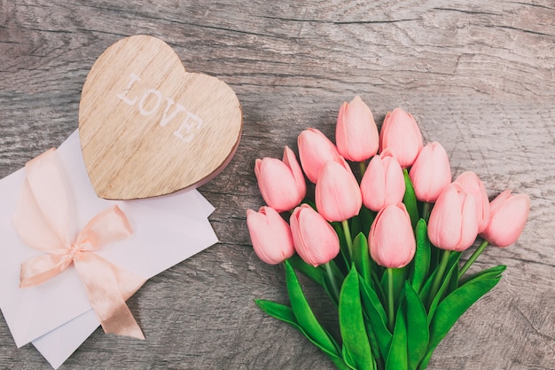 Strauß Tulpen und ein Umschlag auf einem hölzernen Hintergrund, Draufsicht.