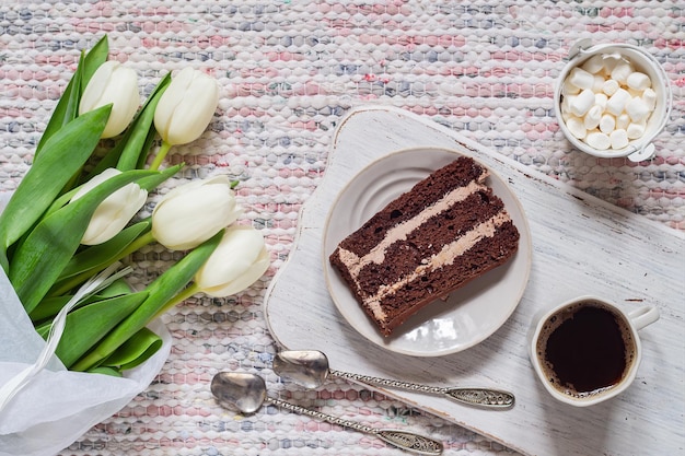 Strauß weißer Tulpen, Kaffee und Schokoladenkuchen auf Textilhintergrund