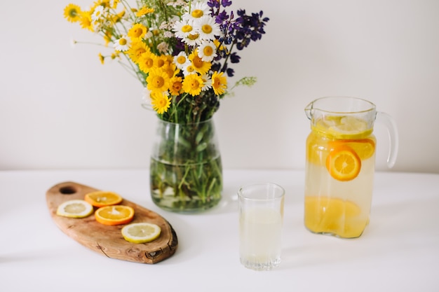 Strauß wilder Naturblumen in einer Vase und hausgemachte Limonade mit Orangen und Zitronen