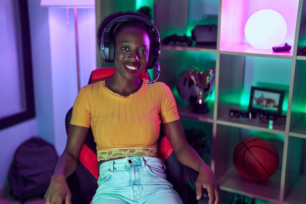 Streamer de mujer afroamericana sonriendo confiada usando auriculares en la sala de juegos