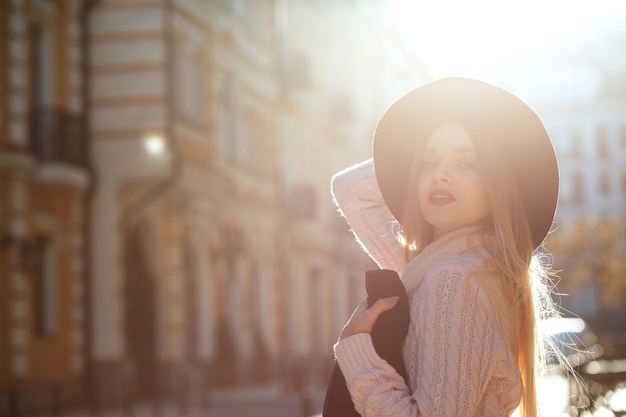 Street-Fashion-Konzept: schönes junges Model mit Hut und Pullover, das mit Sonnenblendung posiert. Platz für Text