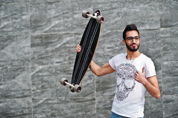 Foto street style arabischer mann in brillen mit longboard gegen graue wand gestellt daumen hoch zeigen