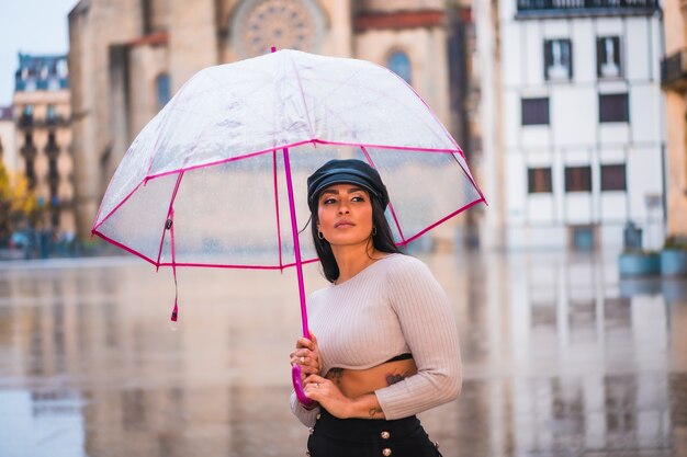 Street style de uma jovem morena na chuva da cidade com um guarda-chuva