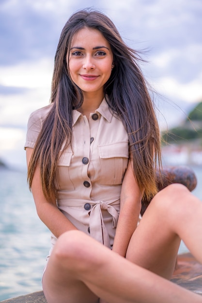 Street style, una joven mujer caucásica morena sentada con un mono corto marrón en verano junto al mar