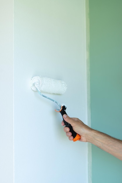 Streichen der Wand mit einer Rolle Mannhand mit Farbrolle Vertikales Foto