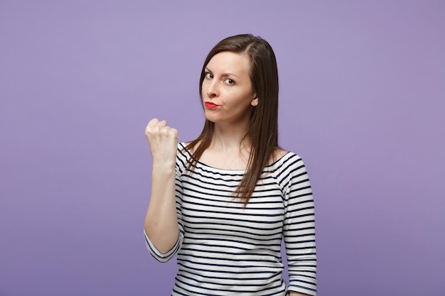 Strenge wütende junge brünette Frau in lässig gestreifter Kleidung posiert isoliert auf violett-violettem Hintergrund Studioportrait. People-Lifestyle-Konzept. Mock-up-Kopienbereich. Kamera suchen, Faust ballen.