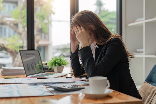 Stress, Angst und Erschöpfung bei einer Geschäftsfrau, die am Arbeitsplatz einen Laptop benutzt, während sie an Kopfschmerzen leidet