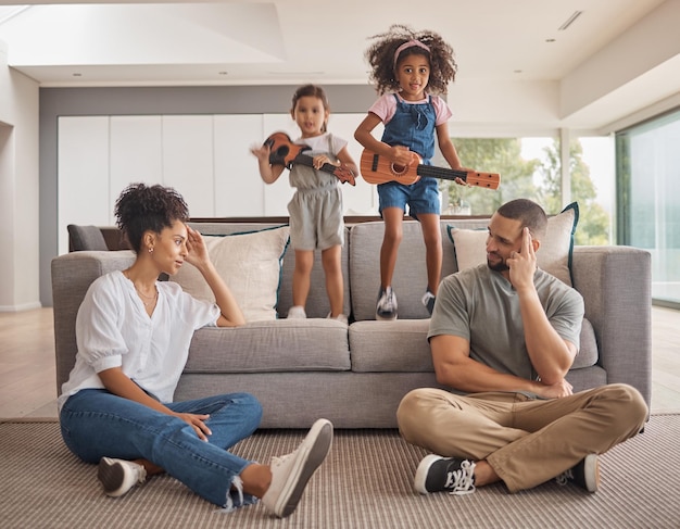 Stress Familie und Energie mit Kindern, die im Wohnzimmer zu Hause Musik auf einer Gitarre spielen, während sie Mama und Papa Kopfschmerzen bereiten Psychische Gesundheit Kinder und müde mit einem Mädchen und einer Schwester, die Chaos verursachen