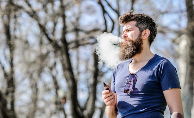 Stressabbau-Konzept. Bärtiger Mann, der Vape raucht. Weiße Wolken aus aromatisiertem Rauch. Elektronische Zigarette rauchen. Mann langer Bart entspannt mit Rauchgewohnheit. Mann mit Bart und Schnurrbart atmet Rauch aus.