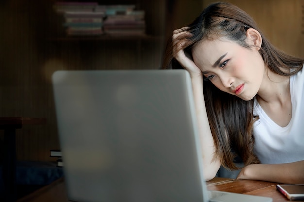 Stressige asiatische Frau, die im Büro sitzt und Laptopschirm betrachtet.