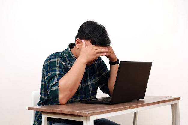 Stresster, frustrierter junger asiatischer College-Student sitzt und benutzt einen Laptop auf dem Schreibtisch