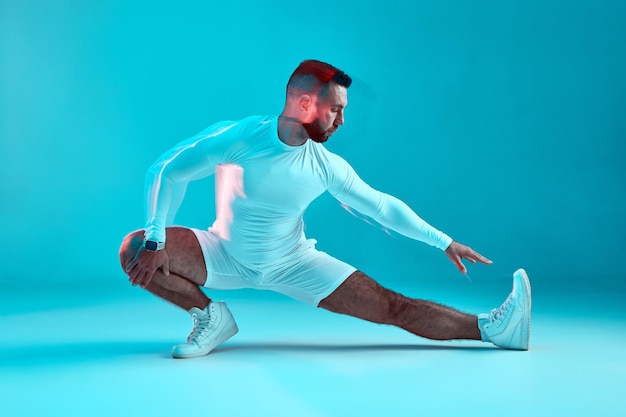 Stretching-Training, athletischer, flexibler junger Mann, Fitnesstrainer, dehnt die Beinmuskulatur auf Blau