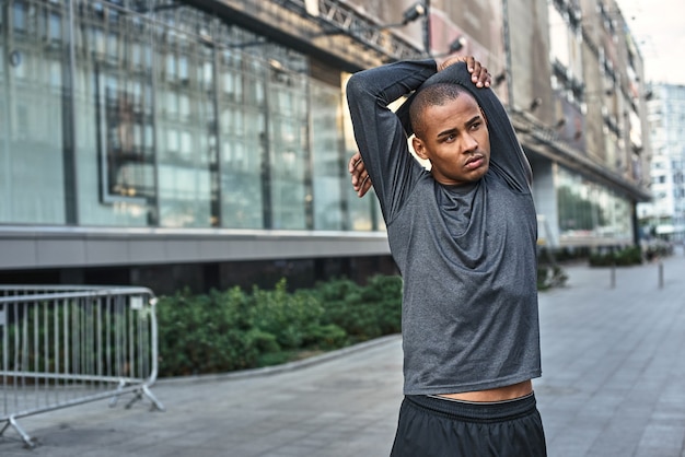 Foto stretching vor dem großartigen morgentraining, nahaufnahme des porträts eines athletischen afrikanischen mannes, der draußen steht