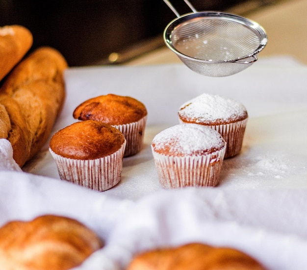 Streuen Sie Cupcakes mit Zuckerpulver durch ein Sieb