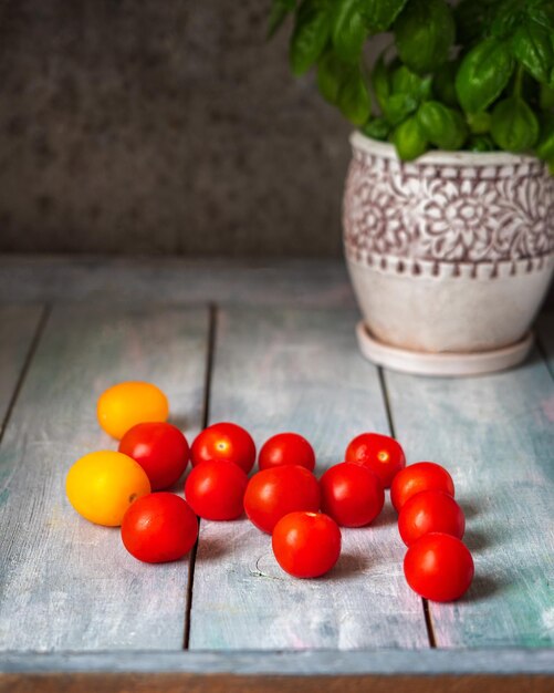 Foto streuen sie reife tomaten auf einen holztisch und basilikum in einem dekorativen blumentopf