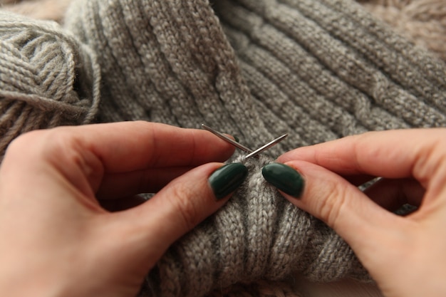 Stricken - die Hände der jungen Frau mit Stricknadeln und grauer Wollrolle. Frauenhände stricken Schal