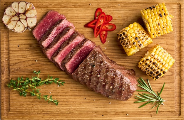 Striploin raro assando carne tenra e suculenta fatiada com condimentos espiga de milho, alho e pimenta