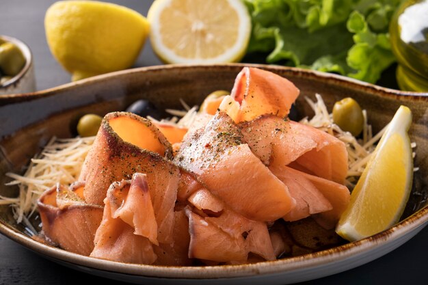 Stroganina de salmão cru congelado fatiado em um prato de queijo, azeitonas e limão. Peixe congelado fatiado.