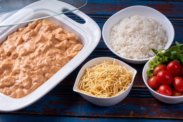 Stroganoff de pollo acompañado de arroz, ensalada y pajita.