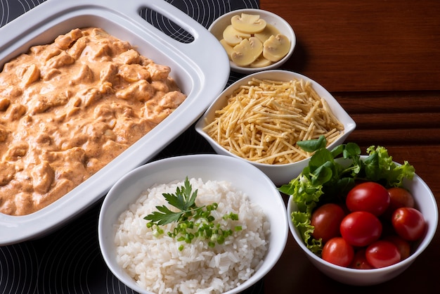 Stroganoff de pollo acompañado de arroz, ensalada y pajita.