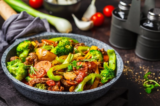 Stroganoff de ternera frito con patatas, brócoli, maíz, pimiento, zanahorias y salsa en una sartén