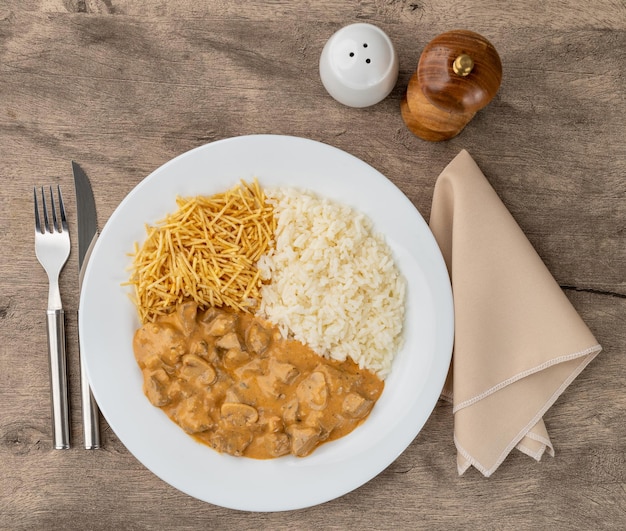 Strogonoff de carne con arroz y patata paja sobre mesa de madera