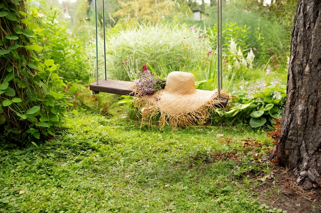 Foto strohhut auf einer schaukel mit blumen auf einem natürlichen grünen hintergrund