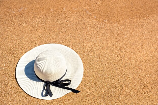 Strohhut der weißen Frau, der auf tropischen Sandstrand am sonnigen Sommertag legt. Urlaubs- und Reisezielkonzept.