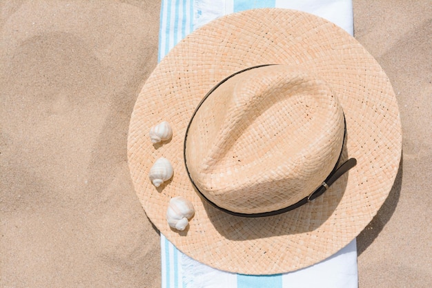 Strohhut mit Muscheln und Strandtuch auf Sand Draufsicht Platz für Text