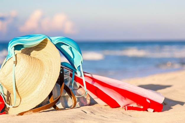 Strohhut, Regenschirm und blauer Bikini-BH-Badeanzug mit Strandtasche am Strand