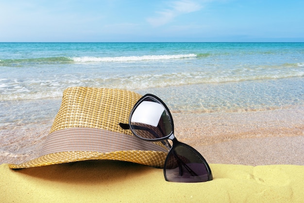 Strohhut und Sonnenbrille auf einer Vorderansicht des Sandstrandes