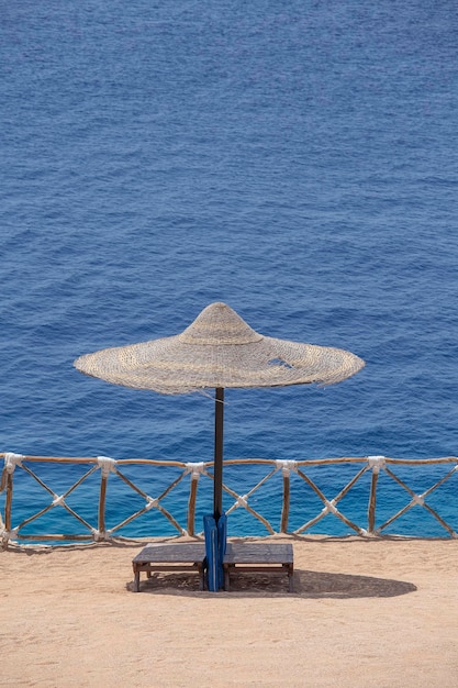 Strohschirme mit Sonnenliegen aus Holz neben dem Roten Meer am Sandstrand im Resort in Sharm El Sheikh Ägypten