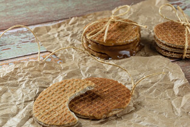 Stroopwafel com uma mordida em papel pardo ao lado de outro biscoito e barbante de sisal (vista lateral).