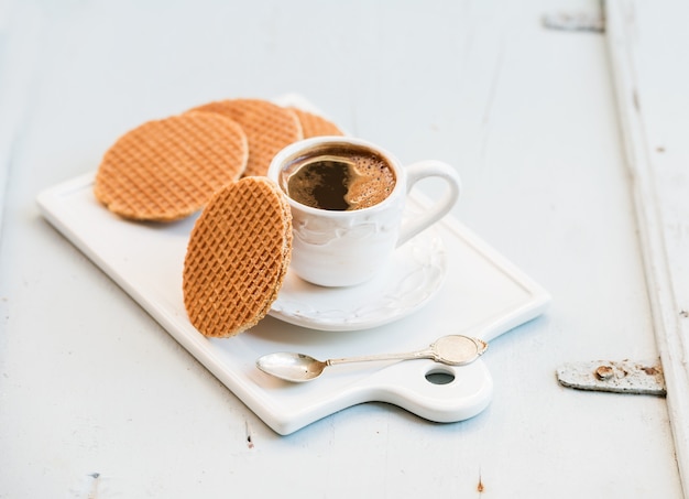 Stroopwafels de caramelo holandés y una taza de café negro sobre una mesa de cerámica blanca sobre una mesa de madera azul claro