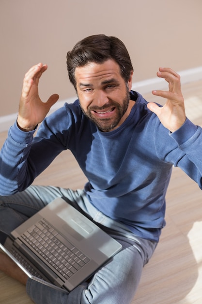 Strssed homem sentado no chão usando laptop em um quarto vazio