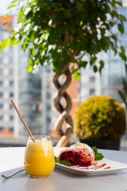 Strudel austríaco tradicional caseiro com cereja ou frutas vermelhas e açúcar em pó com copo de suco de laranja. Menu para café. Fundo brilhante.