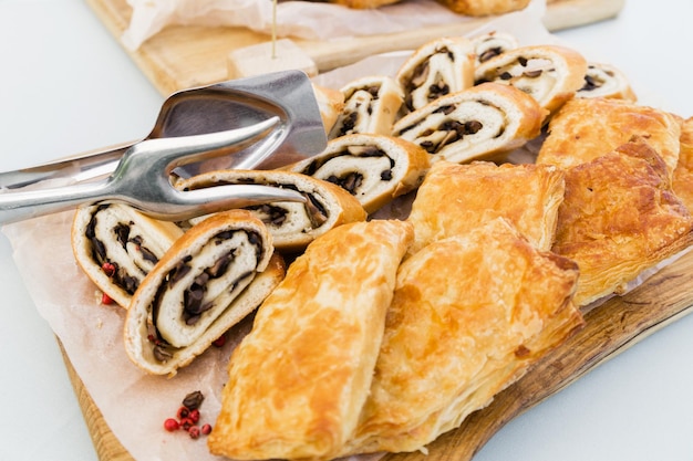 Strudel com cogumelos e folhado com frango e legumes em uma mesa de banquete Há pinças de metal ao lado do lanche Foto horizontal