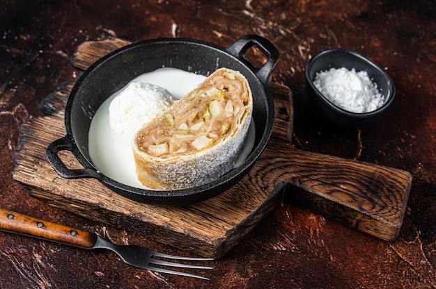 Strudel de apfelstrudel com canela, açúcar de confeiteiro e sorvete de baunilha em uma panela. Fundo escuro. Vista do topo.