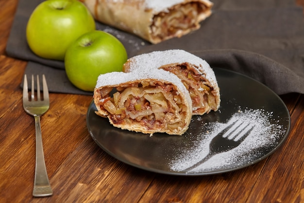 Strudel de maçã com açúcar em pó na chapa preta, mesa de madeira