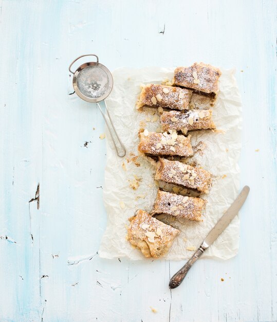 Strudel de manzana y almendras casero sobre papel de hornear sobre fondo de madera azul claro