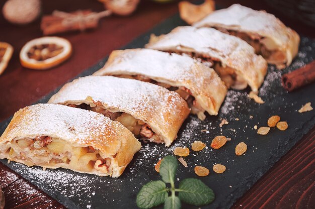 Strudel mit Äpfeln, Rosinen und Walnüssen im rustikalen Stil auf dunklem Hintergrund