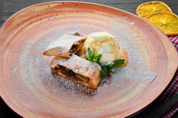 Strudel mit Äpfeln und Eis auf einem Teller Dessert auf einem hölzernen Hintergrund Freier Kopierbereich Ansicht von oben