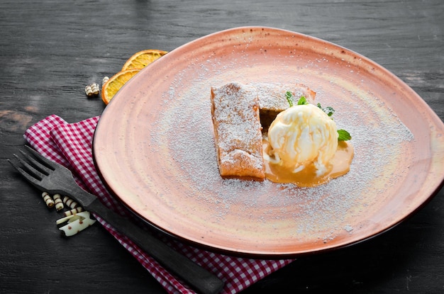 Strudel mit Äpfeln und Eis auf einem Teller Dessert auf einem hölzernen Hintergrund Freier Kopierbereich Ansicht von oben