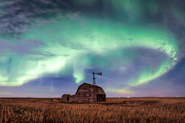 Strudel von hellen Nordlichtern über Weinlesescheune, Behältern, Windmühle und Stoppeln in Saskatchewan, Kanada