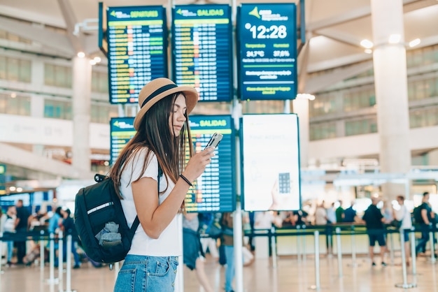 Student am Flughafen an der Anzeigetafel schaut auf das Telefon