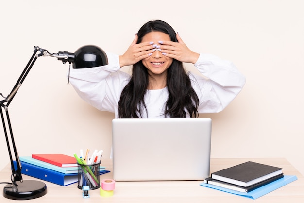 Student asiatisches Mädchen in einem Arbeitsplatz mit einem Laptop lokalisiert auf beige Wand, die Augen durch Hände bedeckt