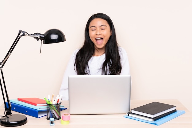 Student asiatisches Mädchen in einem Arbeitsplatz mit einem Laptop lokalisiert auf beige Wand, die nach vorne mit offenem Mund schreit